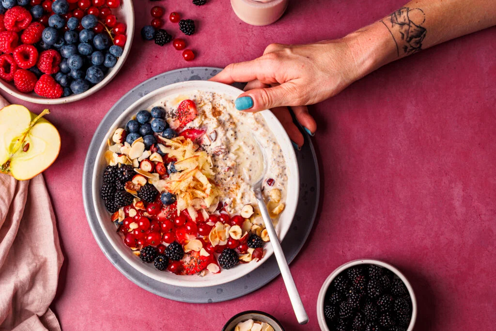 Hand an einer Schüssel mit proteinreichem Bircher Müsli – fotografiert aus der Vogelperspektive.