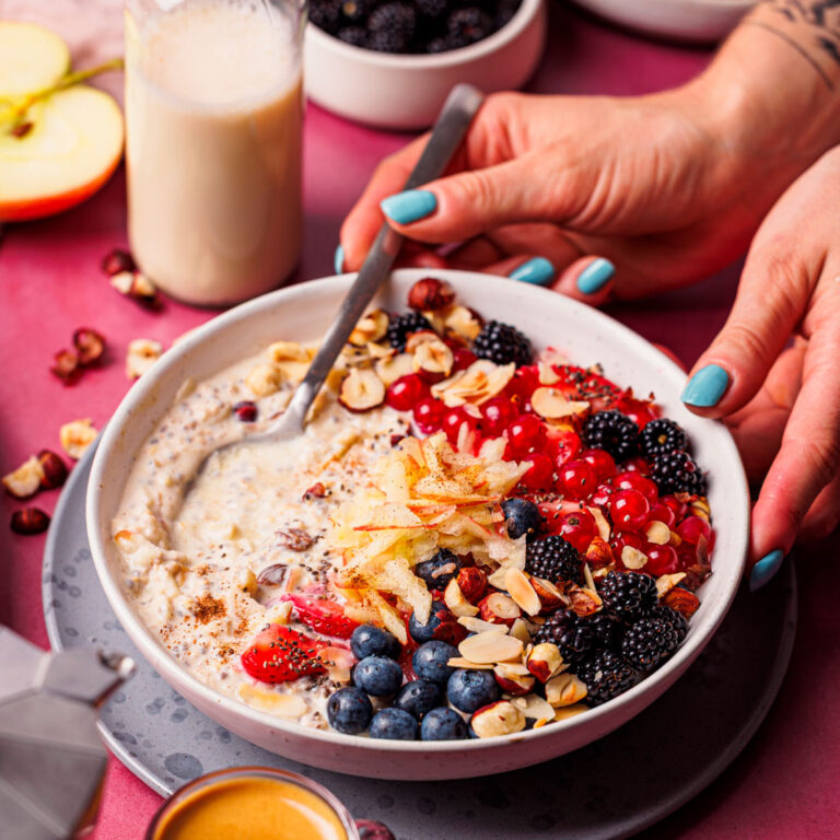 Hände mit Löffel an einer Schüssel High Protein Bircher Müsli mit Beeren.