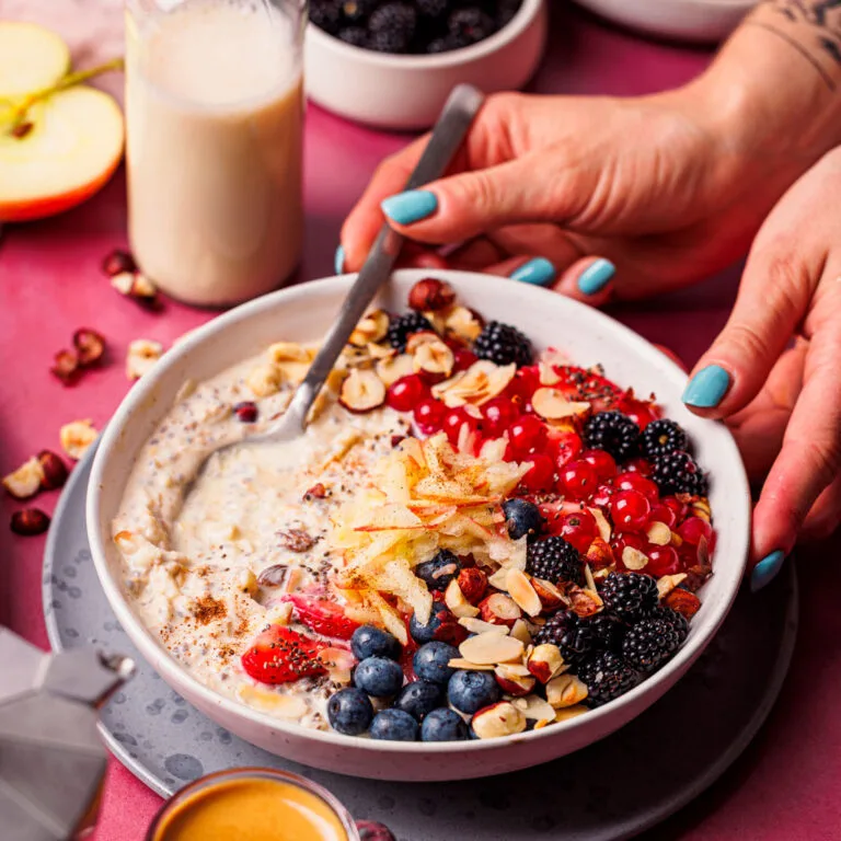 Hände mit Löffel an einer Schüssel High Protein Bircher Müsli mit Beeren.