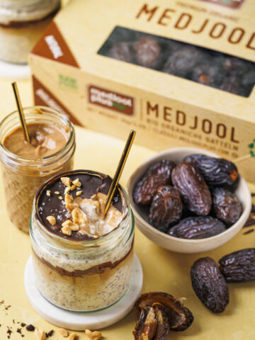 Ein Glas Snickers Overnight Oats mit geknackter Schokoschicht, unter der Dattel-Karamell und die cremigen Oats zu sehen sind.
