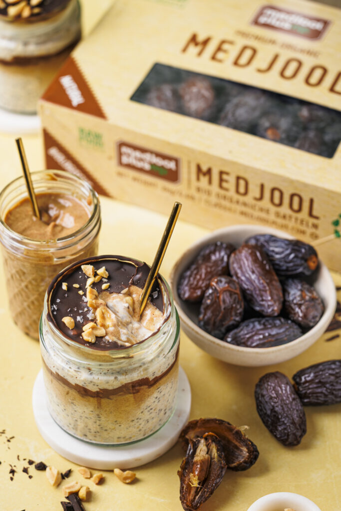 Ein Glas Snickers Overnight Oats mit geknackter Schokoschicht, unter der Dattel-Karamell und die cremigen Oats zu sehen sind.