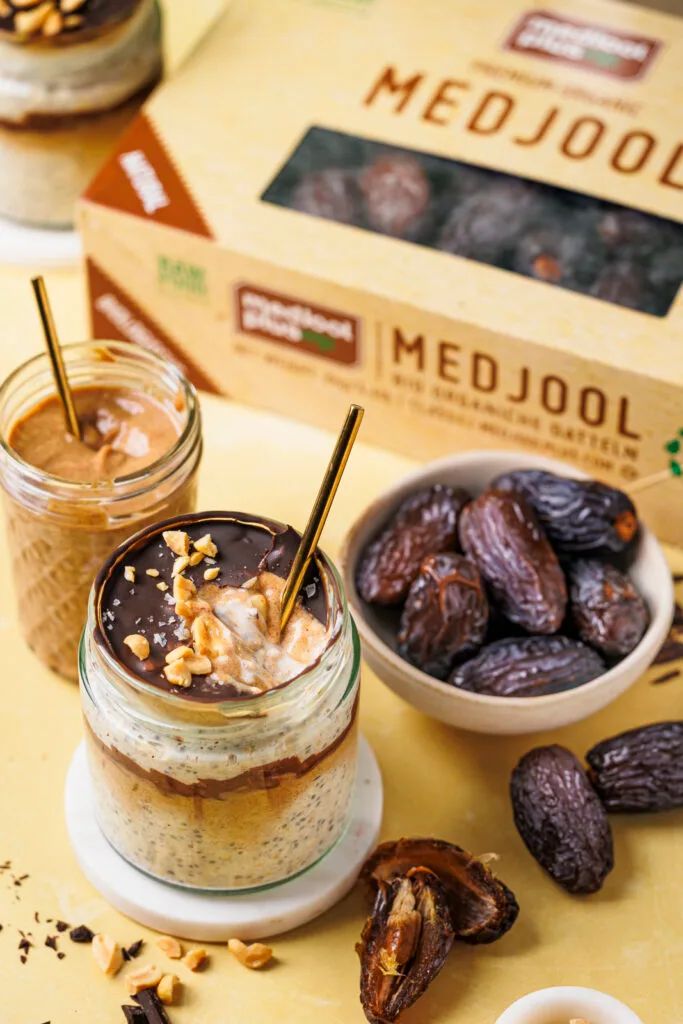Ein Glas Snickers Overnight Oats mit geknackter Schokoschicht, unter der Dattel-Karamell und die cremigen Oats zu sehen sind.