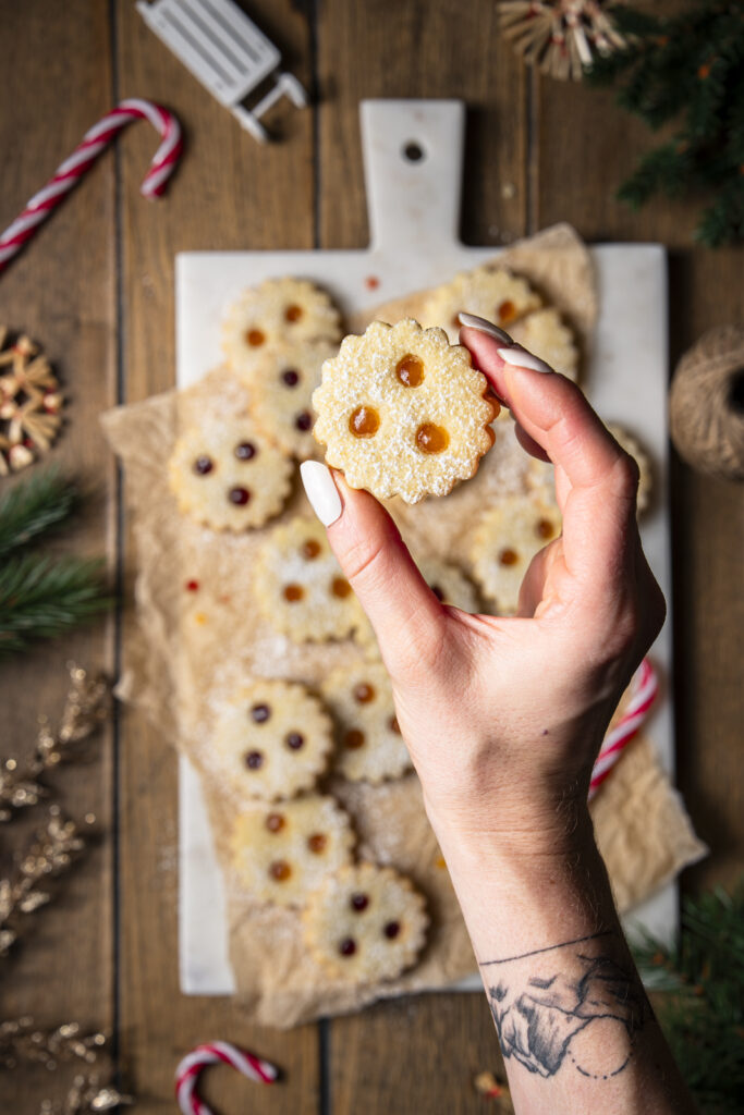 Hand h&auml;lt ein mit Marillenkonfit&uuml;re gef&uuml;lltes und mit Staubzucker bestreutes Linzer Auge (Aufsicht).